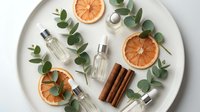 Natural organic cosmetic bottles with dried orange slices, cinnamon sticks and eucalyptus leaves arranged on white ceramic plate for spa wellness beauty.