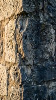 Ancient weathered stone wall with rough textured surface and natural erosion patterns in warm golden sunlight for architectural backgrounds.
