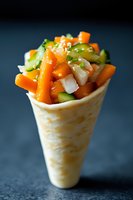 Fresh vegetable wrap cone filled with colorful carrots, cucumber and herbs on dark background for healthy eating and restaurant menu design.
