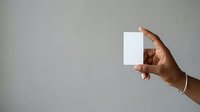 Hand holding blank white card against neutral gray background, ideal for business branding, marketing mockups, and promotional material presentations.