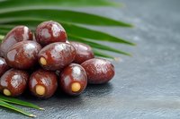 Fresh kalamata olives with green palm leaf on dark slate surface for Mediterranean cuisine and healthy eating concepts.