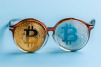Round vintage eyeglasses with golden and silver bitcoin coins seen through lenses on light blue background, creative cryptocurrency concept composition.