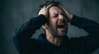 Middle-aged Caucasian man experiencing intense emotional breakdown, screaming with hands on head against dark moody background for mental health concepts.