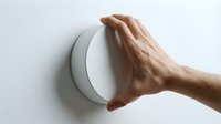 Hand adjusting modern white circular thermostat on wall for home temperature control and energy efficiency in smart house automation system.