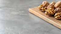 Fresh walnuts on wooden cutting board against gray concrete background with copy space for text. Food photography layout for healthy eating concept.