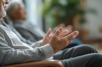 Senior woman's hands resting on wooden armchair during group therapy session, showing emotional gesture while sharing experience in nursing home setting.