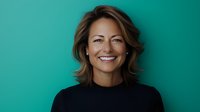 Confident middle-aged woman with bright genuine smile wearing black turtleneck sweater against turquoise background, radiating warmth and professionalism.