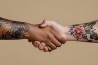 Close-up of tattooed arms with floral designs in handshake gesture against neutral beige background, symbolizing unity, agreement and collaboration.