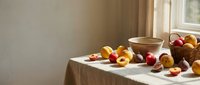 Rustic kitchen table with fresh apricots, cherries and wooden bowls in warm natural sunlight streaming through window creating cozy farmhouse atmosphere.