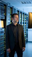 Male IT professional in server room surrounded by data center equipment with illuminated indicator lights, suitable for technology, business, and corporate communications.