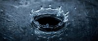 Water splash crown formation on dark wet surface with droplets suspended in motion.