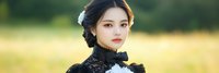 Young Asian woman in elegant black lace Victorian dress with white flower hair accessory posing outdoors in natural golden hour lighting for fashion portrait.