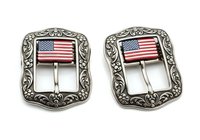 Pair of ornate silver belt buckles featuring American flag design with decorative baroque-style frames, isolated on white background for apparel and accessories design use.