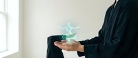 Professional businessman in dark suit holding glowing digital hologram in cupped hands representing innovation, technology and future business concepts.