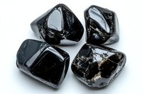 Black tourmaline crystal stones on white background, rough natural mineral specimens with glossy surface showing characteristic striations and fracture patterns.