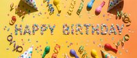Happy birthday celebration flat lay with colorful party hats, confetti, streamers and decorative elements on yellow and orange background for festive occasions.