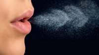 Woman's mouth exhaling visible breath vapor cloud against dark background showing cold air temperature and respiratory droplets in winter weather.