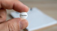 Hand holding white placebo pill tablet between fingers with blurred medical prescription paper in background for pharmaceutical research studies.