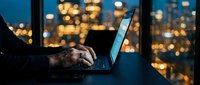 Professional businessman working late on laptop computer in modern office with city lights bokeh background at night for business productivity concepts.