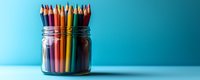 Colorful wooden pencils standing in glass jar against turquoise blue background with copy space. Minimalist creative education concept for art and design.