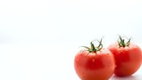 Fresh red tomatoes with green stems on white background for healthy cooking and nutrition concepts.