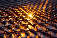 Mesmerizing golden light shimmers through textured metallic surface creating abstract wave pattern with warm orange glow and dramatic shadows in macro photography.
