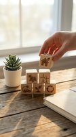 Hand placing wooden cube with house icon on stack of eco-friendly blocks featuring renewable energy symbols on rustic table near window with succulent plant.