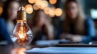 Glowing vintage light bulb on blurred background with warm bokeh lights, illuminating dark workspace atmosphere. Creative business concept for innovation and ideas.