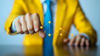 Business professional in yellow suit drawing digital network connection points on transparent surface, demonstrating technology innovation and strategic planning.