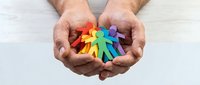Male hands gently holding colorful rainbow paper cutout figures representing diversity, inclusion, unity and community support concepts for social campaigns.