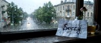 Handwritten sorry note on windowsill with rainy city view, tea, and flower, evoking apology, regret, and emotional mood.