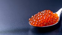 Fresh red caviar on silver spoon against dark background, luxury seafood delicacy with glossy texture and vibrant orange color, gourmet appetizer presentation.