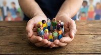 Hands holding diverse group of colorful wooden people figures representing community unity, teamwork and inclusion concepts for social projects.