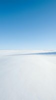 Minimalist winter landscape with pristine snow-covered terrain and a thin blue water line dividing the composition under clear sky. Suitable for backgrounds and serene nature concepts.