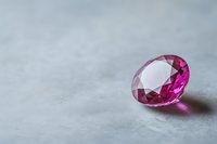 Vibrant pink gemstone on light gray background showcases brilliant cut facets and crystal clarity, casting subtle reflections. Luxury jewelry concept.
