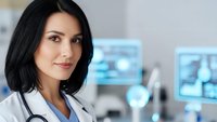 Professional female doctor with stethoscope smiling confidently in modern medical office environment for healthcare and medical consultation concepts.
