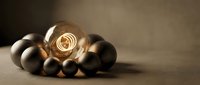 Glowing light bulb surrounded by metallic spheres on neutral surface, representing innovation, leadership, and creative business solutions.
