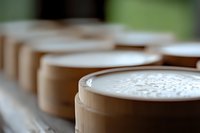 Fresh creamy latte drinks with milk foam in brown paper cups lined up on counter, shallow depth of field creates soft blurred background effect.