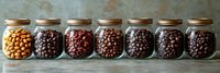 Coffee beans in glass jars showing roasting progression from light to dark, arranged in row on rustic wooden surface, demonstrating coffee roasting stages.