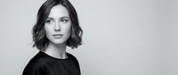 Professional portrait of confident young Caucasian woman with short wavy bob haircut wearing black top against neutral background for business marketing.