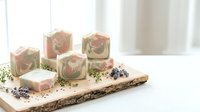 Handmade natural soap bars with rose petals and lavender sprigs arranged on rustic wooden board for spa skincare and aromatherapy wellness routine.