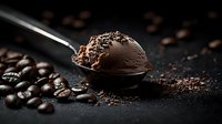 Creamy chocolate ice cream scoop on metal spoon surrounded by scattered coffee beans on dark textured background, moody food photography composition.