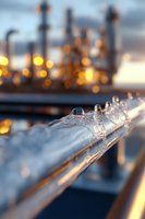 Frozen ice formations on metal railing during winter sunset with industrial facility and glowing lights in blurred background creating atmospheric mood.
