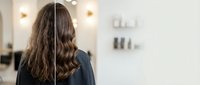 Professional woman with long wavy brown hair wearing headphones in modern office environment, remote work and communication concept.