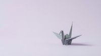 Origami paper crane folded from white sheet on soft lavender background, isolated for design projects, crafts, and creative compositions.