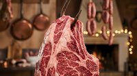 Raw beef steak hanging with festive decorations and warm lights, suitable for butcher shop promotions, holiday meat sales, and culinary marketing materials.