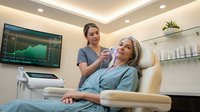 Female dentist examining blonde patient in modern dental office with advanced equipment and monitor displaying dental imaging.