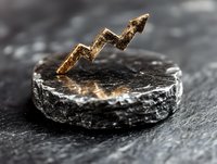 Golden arrow chart on black stone base showing upward trend against dark background, representing financial growth and market success concept.