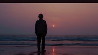 Silhouette of person standing alone on beach at sunset, watching sun sink into ocean horizon with reflection on wet sand, creating atmospheric seascape scene.