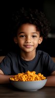 Adorable African American boy with curly hair enjoying bowl of macaroni and cheese at table wearing dark shirt smiling at camera for family dining content.